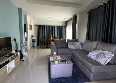 Modern living room with a grey sectional sofa, TV, and dining area in the background