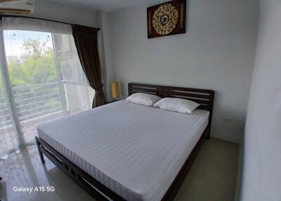 A bedroom with a large bed, artwork above the bed, and a window with curtains and a balcony view.