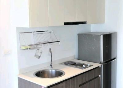 Modern compact kitchen with wooden lower cabinets, stainless steel sink, countertop stove, and refrigerator.