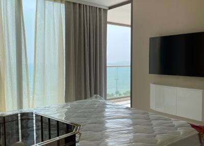 Modern bedroom with large window, ocean view, wall-mounted TV, and a bed covered in plastic.