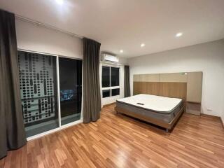 Spacious bedroom with wooden floor and large bed next to windows.