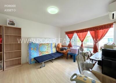 Living room with wooden floor, sofa bed, bookshelf, large windows with curtains, and various furnishings.