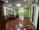 Spacious living room with wooden floor, green accent wall, and large windows