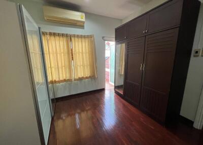 A bedroom with hardwood floors, a large wardrobe, and window with curtains