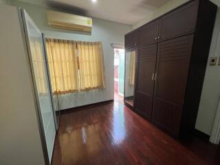 A bedroom with hardwood floors, a large wardrobe, and window with curtains