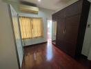 A bedroom with hardwood floors, a large wardrobe, and window with curtains