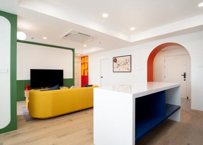 Living room with modern decor featuring a yellow sofa, television, artistic wall decor, and a countertop with shelves.