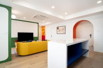 Living room with modern decor featuring a yellow sofa, television, artistic wall decor, and a countertop with shelves.