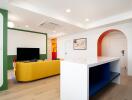 Living room with modern decor featuring a yellow sofa, television, artistic wall decor, and a countertop with shelves.