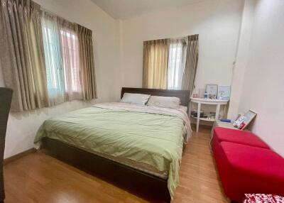 Bedroom with double bed, wooden floor, red bench, and windows with curtains.