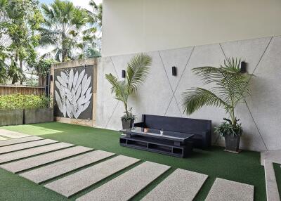 Modern outdoor seating area with green artificial grass, potted plants, and a wall art