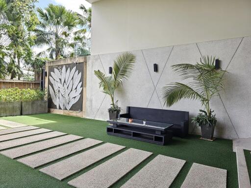 Modern outdoor seating area with green artificial grass, potted plants, and a wall art