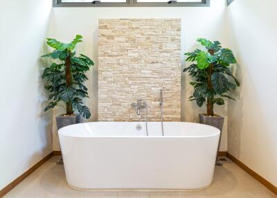 Modern bathroom with freestanding bathtub, stone accent wall, and potted plants