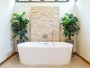 Modern bathroom with freestanding bathtub, stone accent wall, and potted plants