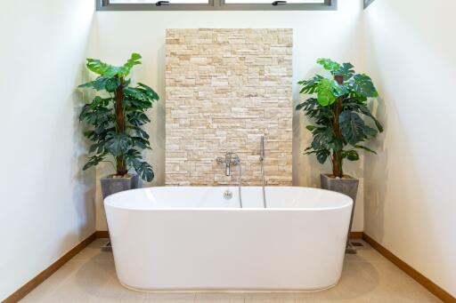 Modern bathroom with freestanding bathtub, stone accent wall, and potted plants