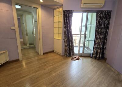 A bedroom with wooden flooring, built-in shelves, and a sliding glass door leading to a balcony.