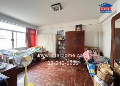 A bedroom with two beds, wooden flooring, a fan, cabinets, and various personal items.