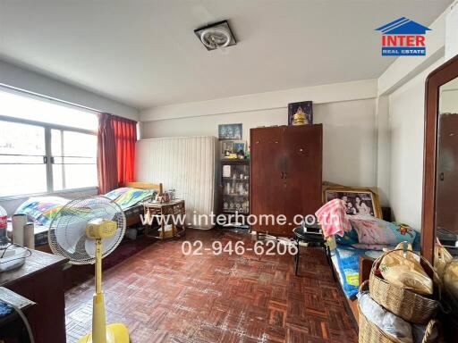 A bedroom with two beds, wooden flooring, a fan, cabinets, and various personal items.