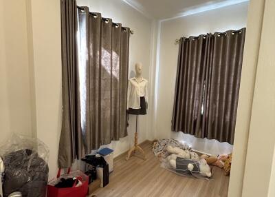 A small bedroom with curtained windows, mannequin, and scattered belongings