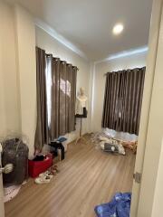 A small bedroom with curtained windows, mannequin, and scattered belongings