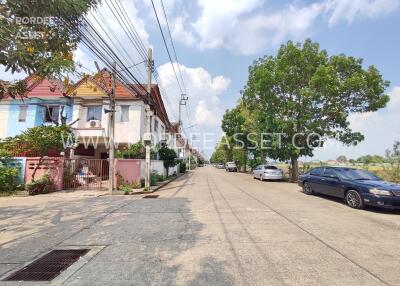 Street view with houses, trees, and parked cars on a sunny day