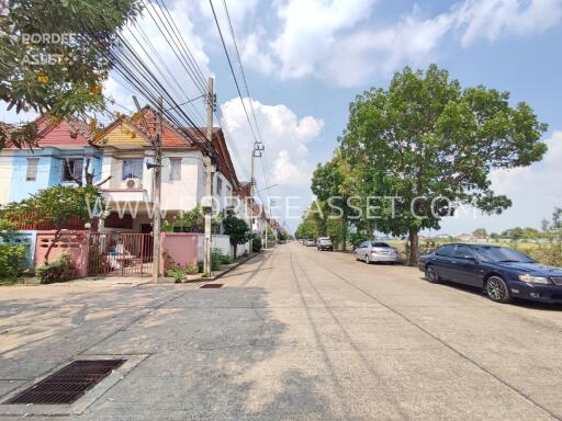 Street view with houses, trees, and parked cars on a sunny day