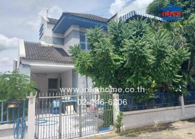 Front exterior view of a two-story residential house with gated entrance and surrounding greenery.