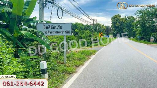 Road view with greenery along the side and a sign welcoming visitors