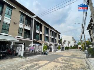 A street view of a multi-story residential building with balconies and a gated entrance.