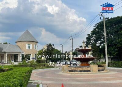 A scenic view of a residential area featuring a pathway, green landscaping, and a large central fountain.