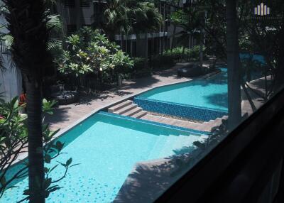 Modern apartment complex outdoor swimming pool area surrounded by lush greenery.