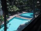 Modern apartment complex outdoor swimming pool area surrounded by lush greenery.