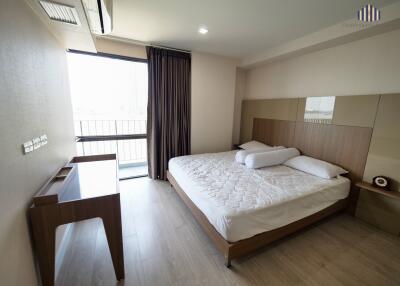 Spacious bedroom with a large bed, desk, and balcony access