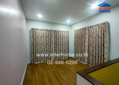 Bedroom with wooden floor, floral curtains, and website information