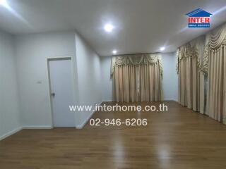 Spacious living room with hardwood floors and large windows with decorative curtains