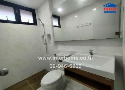 Modern bathroom with white tiles, large mirror, shower, toilet, and sink