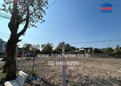 Empty lot with a few trees, surrounded by fencing, and adjacent to a few buildings