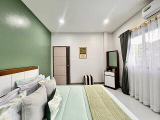 Modern decorated bedroom with a green accent wall, bed, dresser, and window with curtains