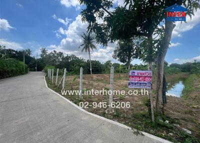 Vacant land plot next to a road with trees and a water feature