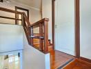 Indoor wooden staircase with white walls and a white door at the top landing