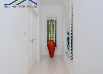 Bright hallway with white walls, a window with blinds, and a decorative red vase with plants