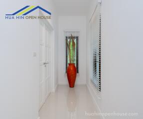 Bright hallway with white walls, a window with blinds, and a decorative red vase with plants