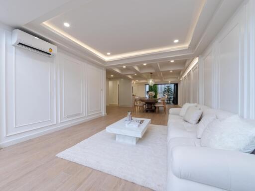 Modern living room with white interior, sofa, coffee table, and dining area in the background