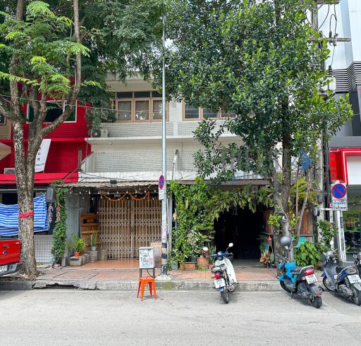 Street view of a commercial building with trees and parked scooters