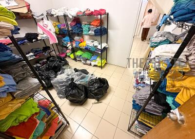 Clothing storage room with shelves full of neatly folded clothes and plastic bags on the tiled floor