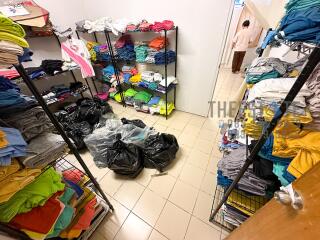 Clothing storage room with shelves full of neatly folded clothes and plastic bags on the tiled floor