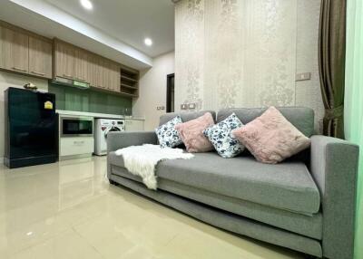 Cozy living room with a grey sofa and a small kitchen in the background