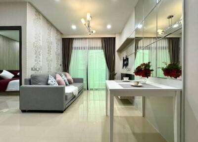 Modern living room with grey sofa, decorative cushions, wall-mounted TV, and dining area