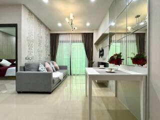 Modern living room with grey sofa, decorative cushions, wall-mounted TV, and dining area