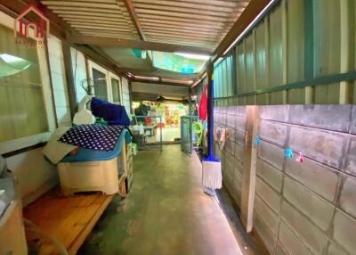 A covered corridor leading to an open area with various household items.